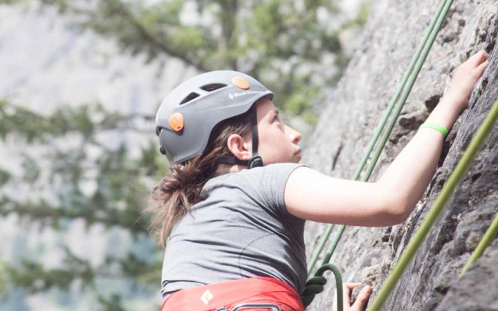 an outward bound student wearing safety gear focuses as they climb a rock facing